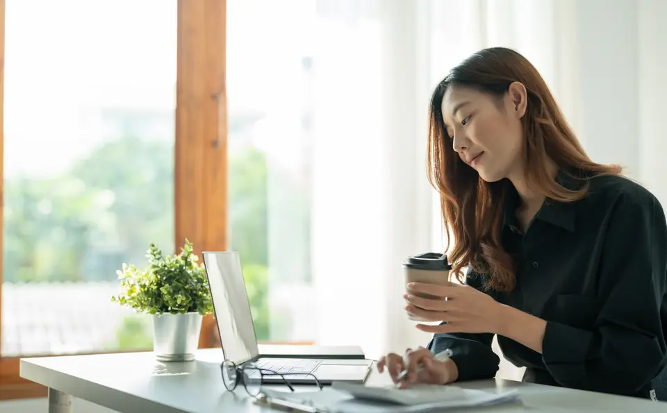 Chủ doanh nghiệp đang kiểm tra website, tay cầm cà phê trong văn phòng sáng